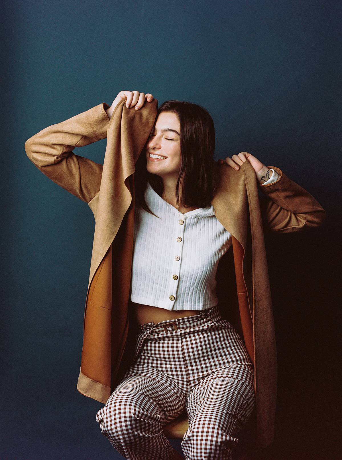 studio portrait on film and contax 645 of model wearing tan tranch coat smiling in front of ultramarine savage seamless paper backdrop