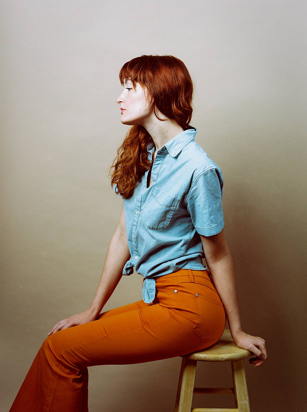studio strobe portrait of girl in earth toned orange and blue clothes and flare jeans shot on kodak portra 160vc expired film