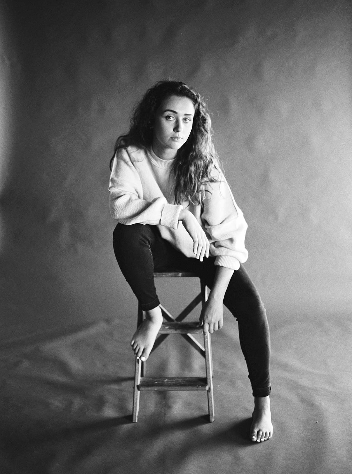 natural light studio portrait on film of girl sitting on stool against savage thunder grey seamless paper backdrop