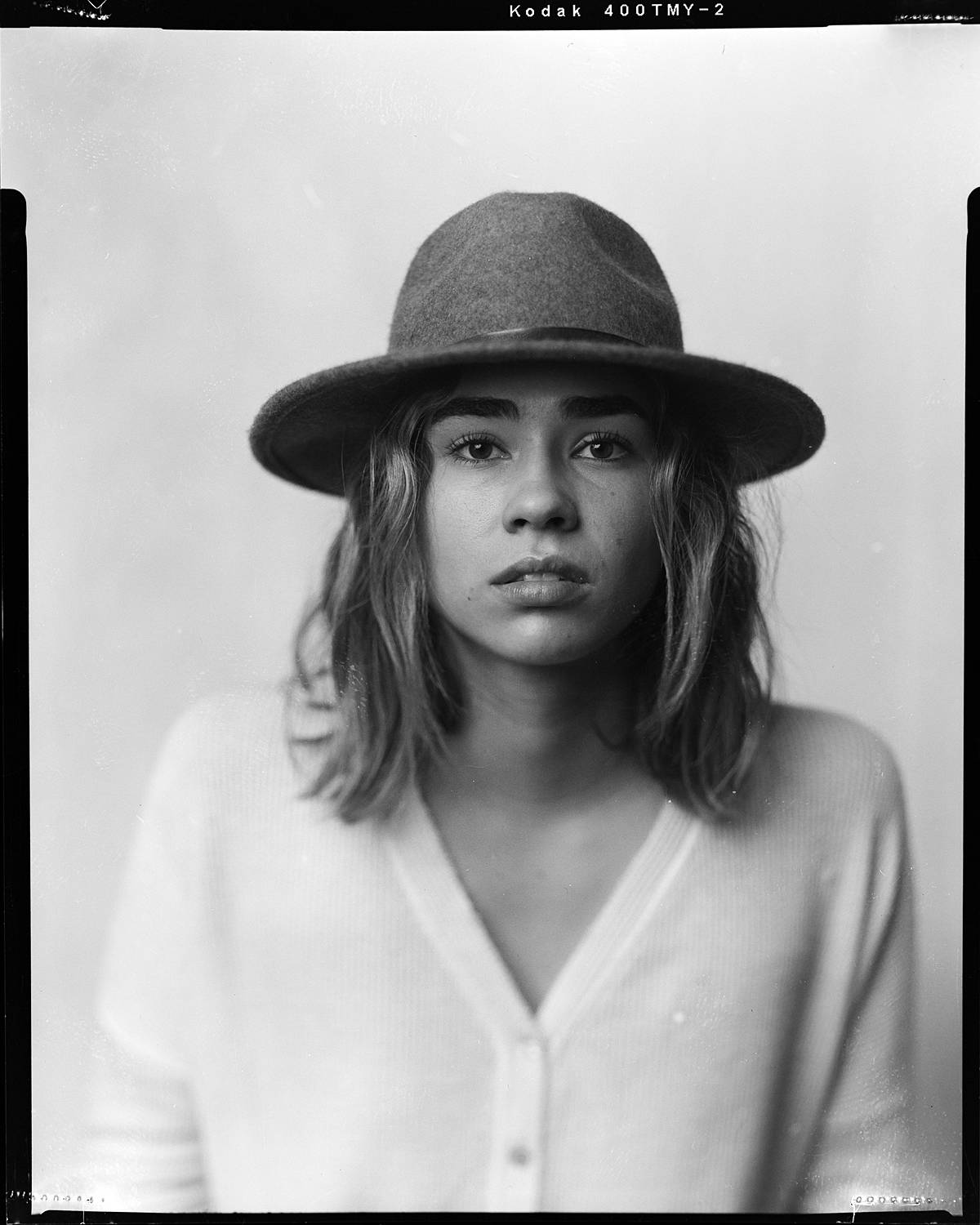 large format film portrait in studio on white backdrop of girl in hat black and white film intrepid 4x5