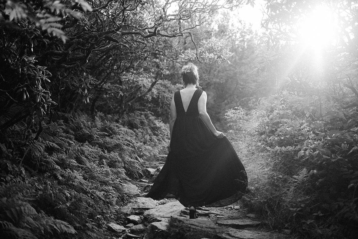 bride hiking up mountain in black dress on blue ridge mountains for destination elopement