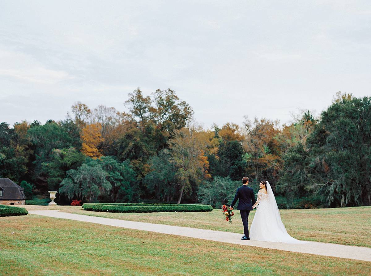 bride and groom walk toward lake at middleton place in charleston south carolina during fall wedding portraits on film