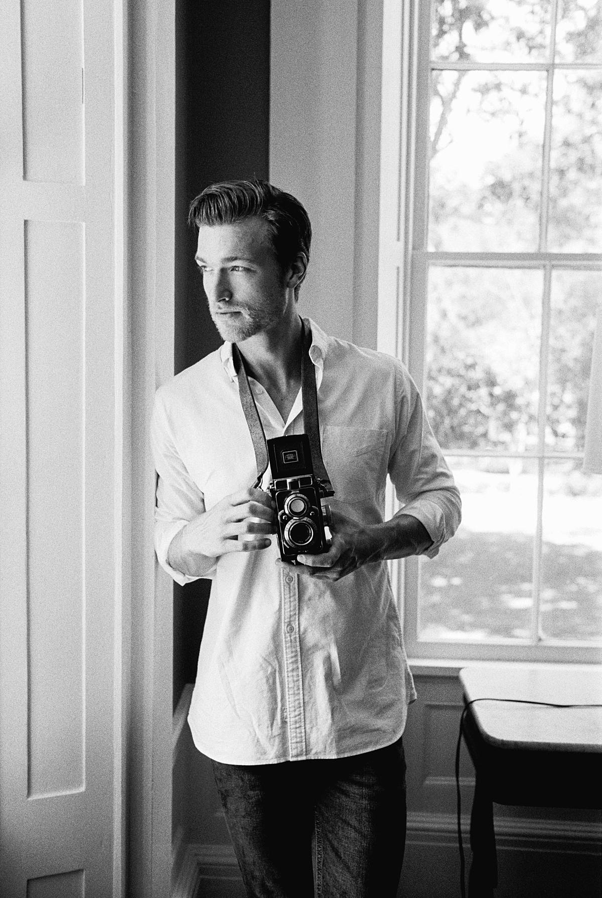 groom holding zeiss tlr on black and white film for south carolina engagement photos at wavering place shot on black and white film