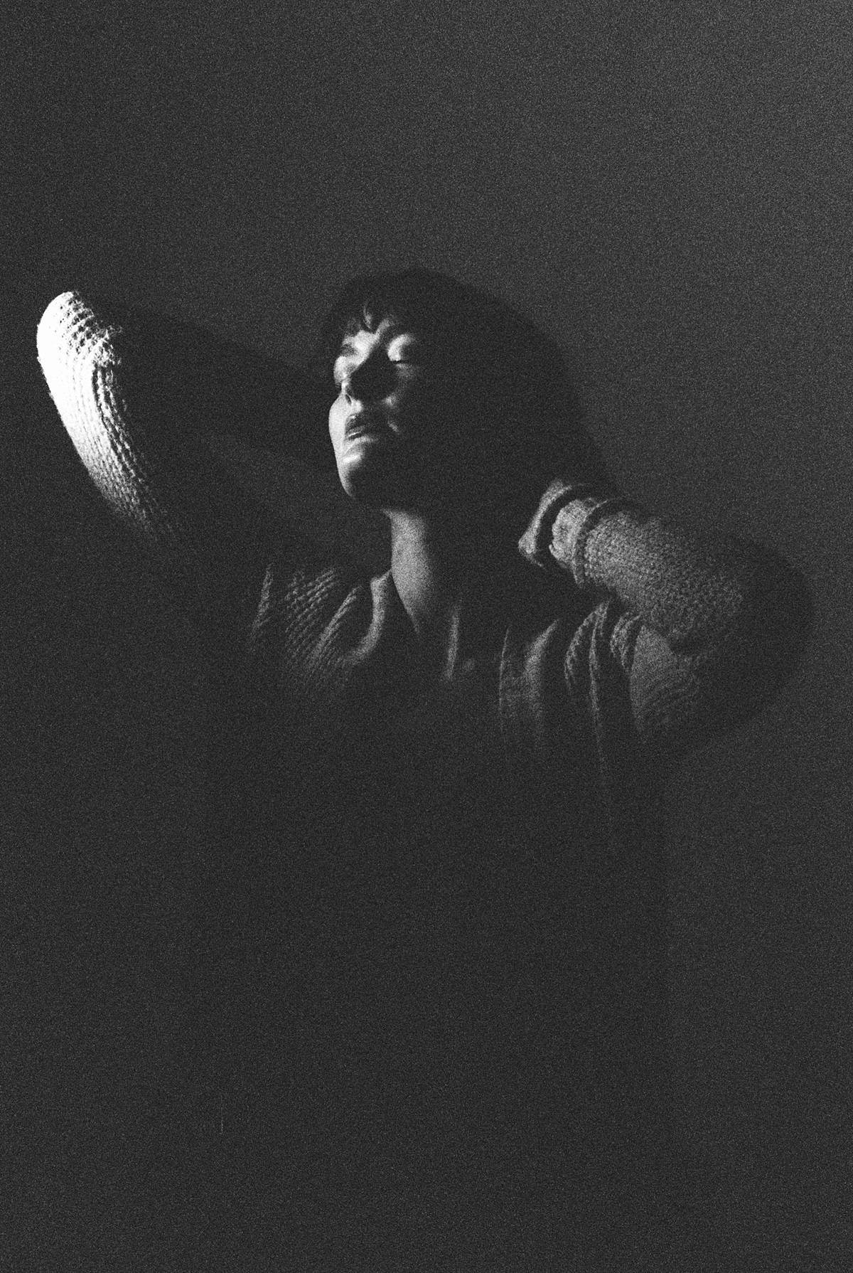 grainy black and white female studio portrait pose with spotlight on face using expired and pushed 35mm black and white film