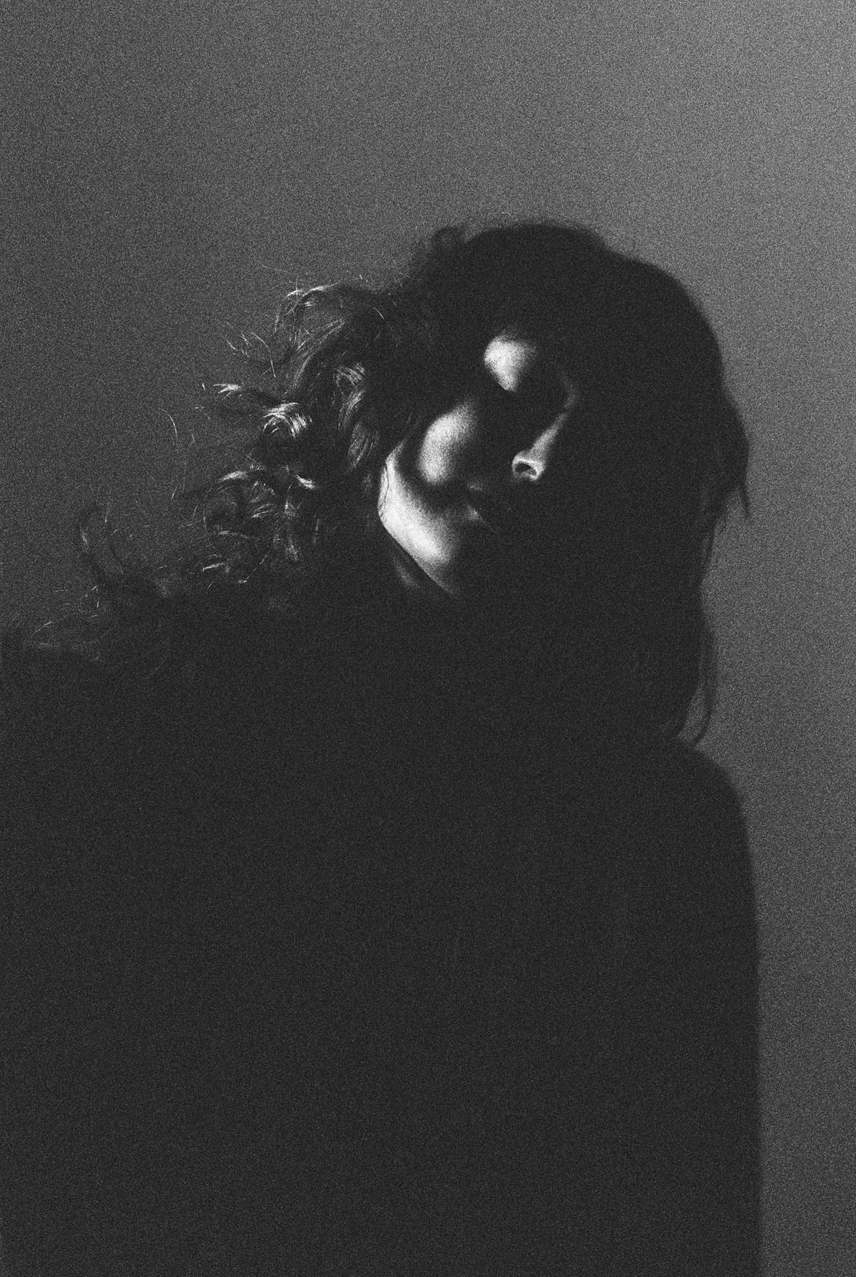 grainy 35mm black and white film portrait of a girl in studio against a black savage seamless paper backdrop